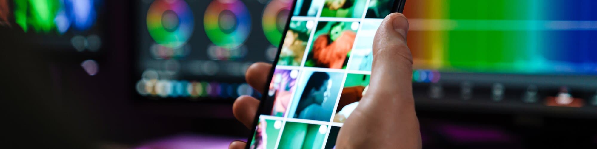Hand holding a phone showing a photo gallery in front of an editing screen