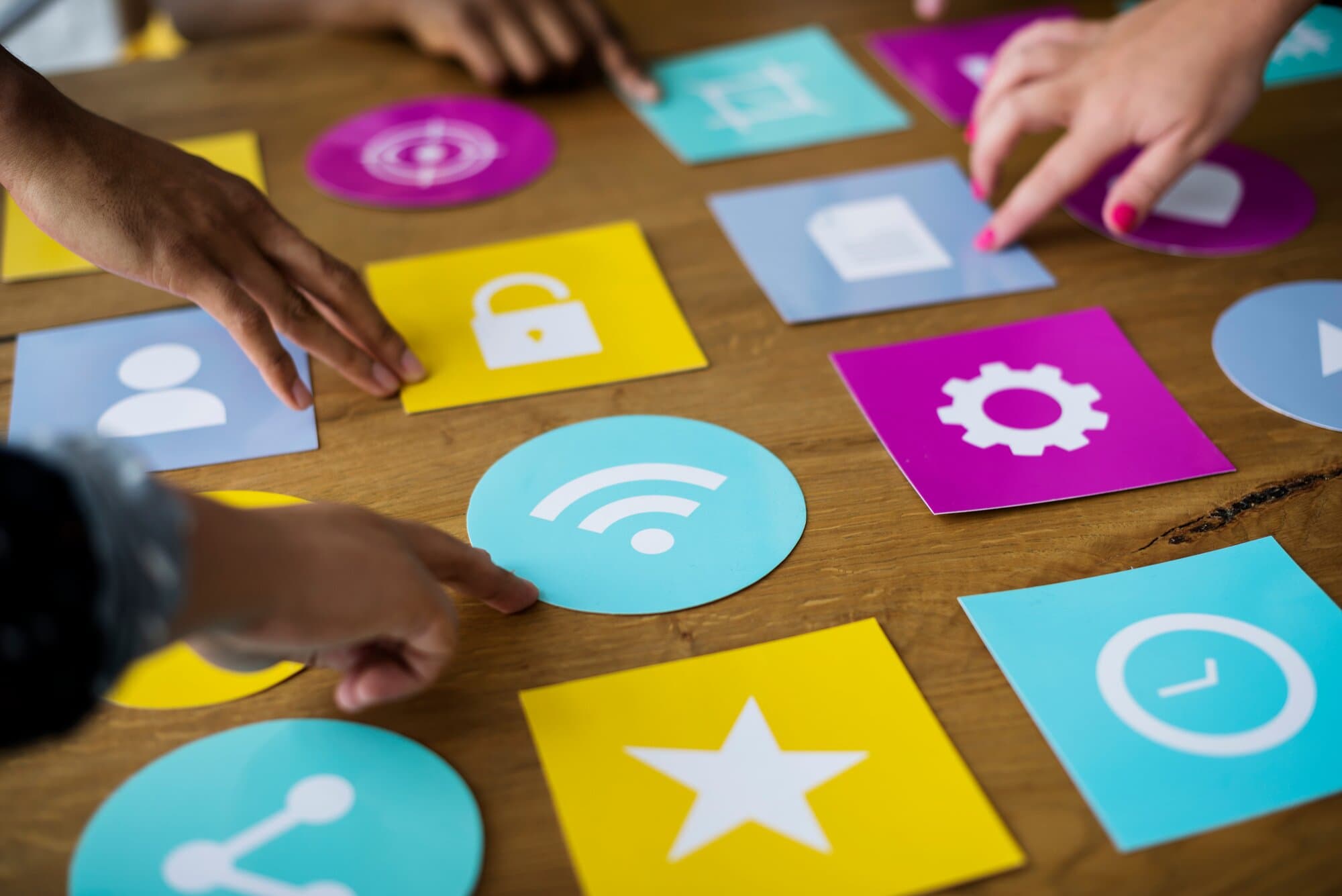 Hands arranging cards of app icons on a table